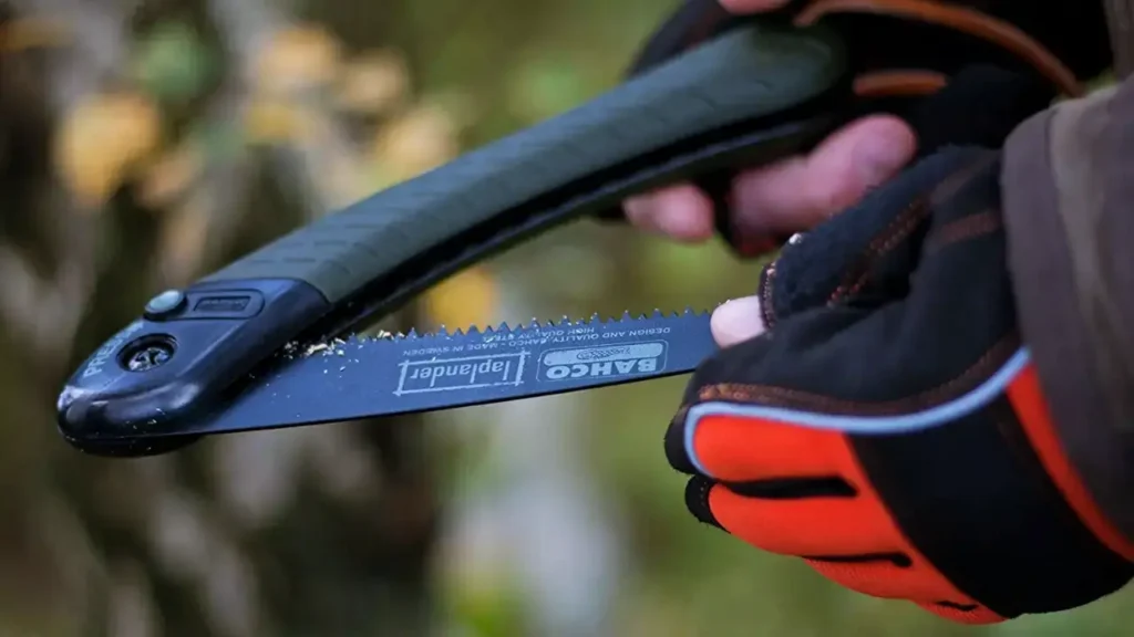 Close-up of the Bahco Laplander Folding Saw with black blade and green handle, shown in hand outdoors during camp wood processing.