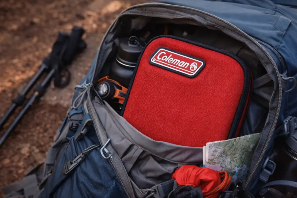 Coleman First Aid Kit tucked into an open hiking backpack as part of a practical camping and trail setup.