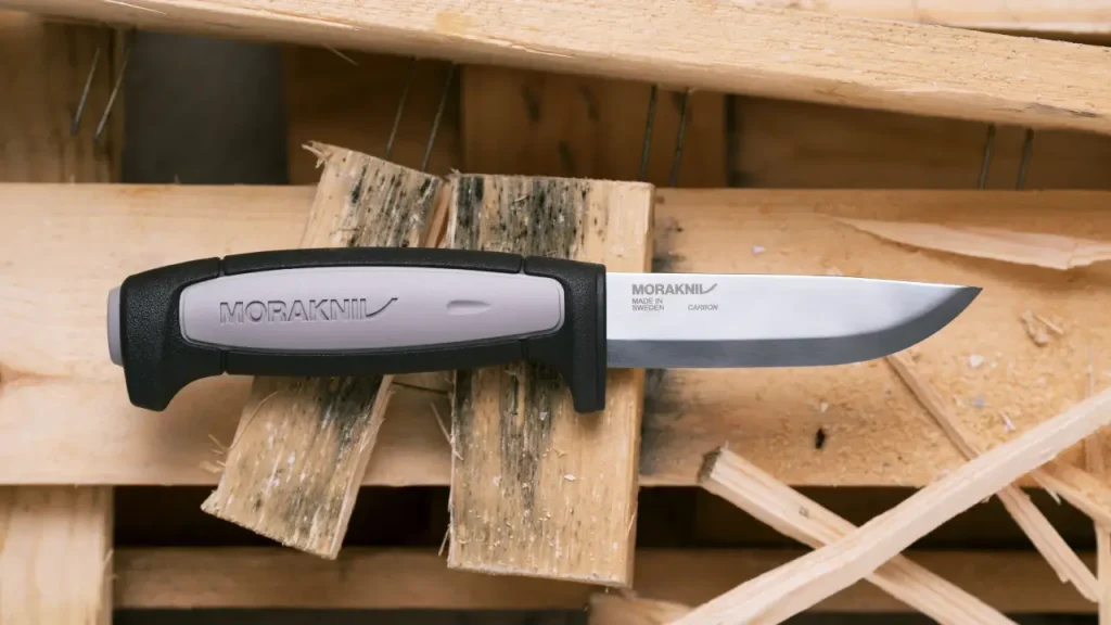 Morakniv Robust Pro carbon steel camping utility knife with a black and gray handle and thick fixed blade resting on split firewood.
