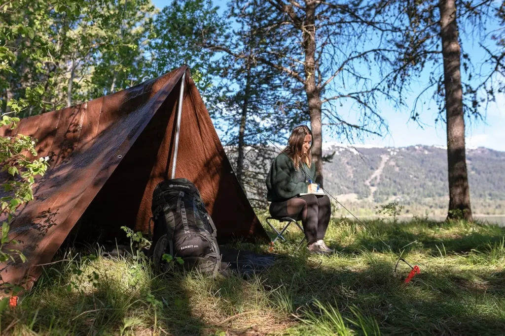 Stansport Tarp pitched as an A-frame camping shelter in a wooded mountain campsite with backpack and camper nearby