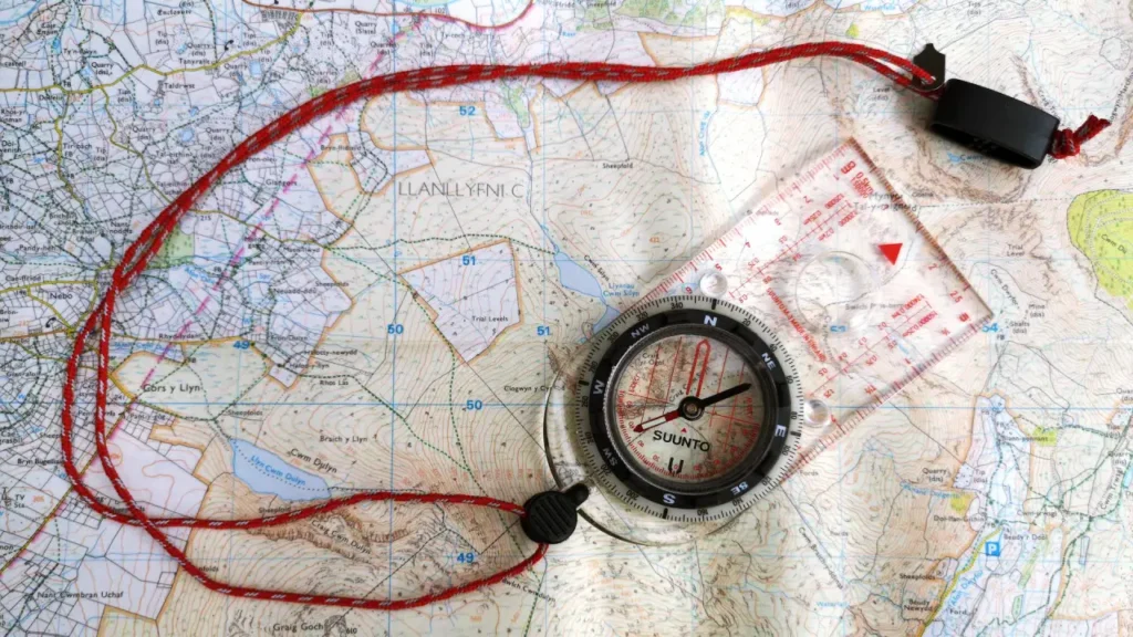 Suunto Compass resting on a topographic map with red lanyard, showing a practical backcountry navigation setup