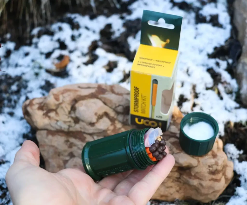 UCO Stormproof Match Kit open in hand outdoors with match case and packaging in a snowy campsite setting.
