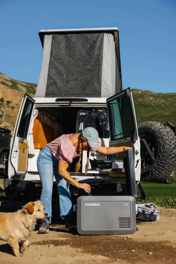 Dometic CFX electric cooler beside a beginner van life setup with rear camp kitchen access, showing practical van life gear for beginners at a mountain campsite.