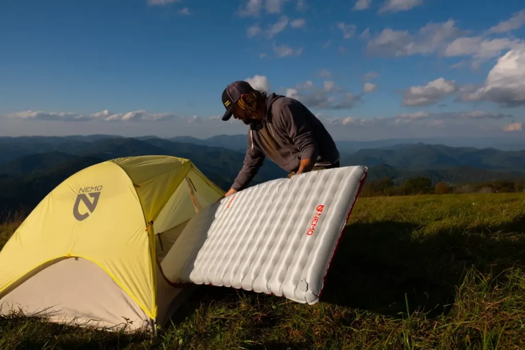 NEMO Tensor All-Season sleeping pad next to a yellow tent at a mountain campsite, representing one of the best sleeping pads for camping comfort and support