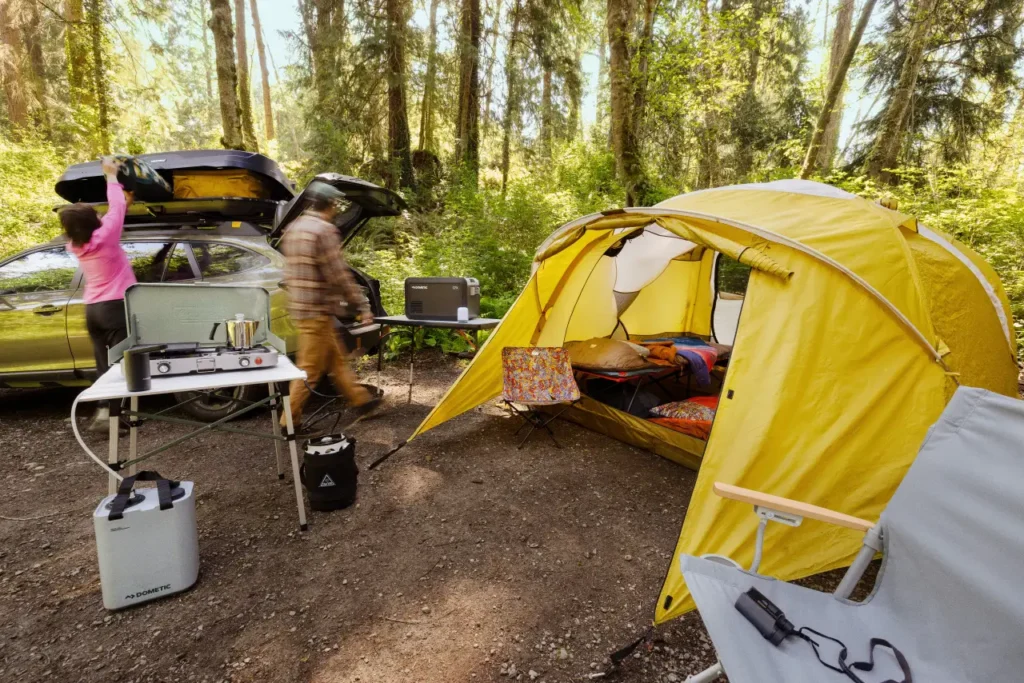REI Co-op Base Camp 4 Tent at a forest car camping campsite with camp stove, Dometic cooler, roof cargo box, and organized weekend camping gear.