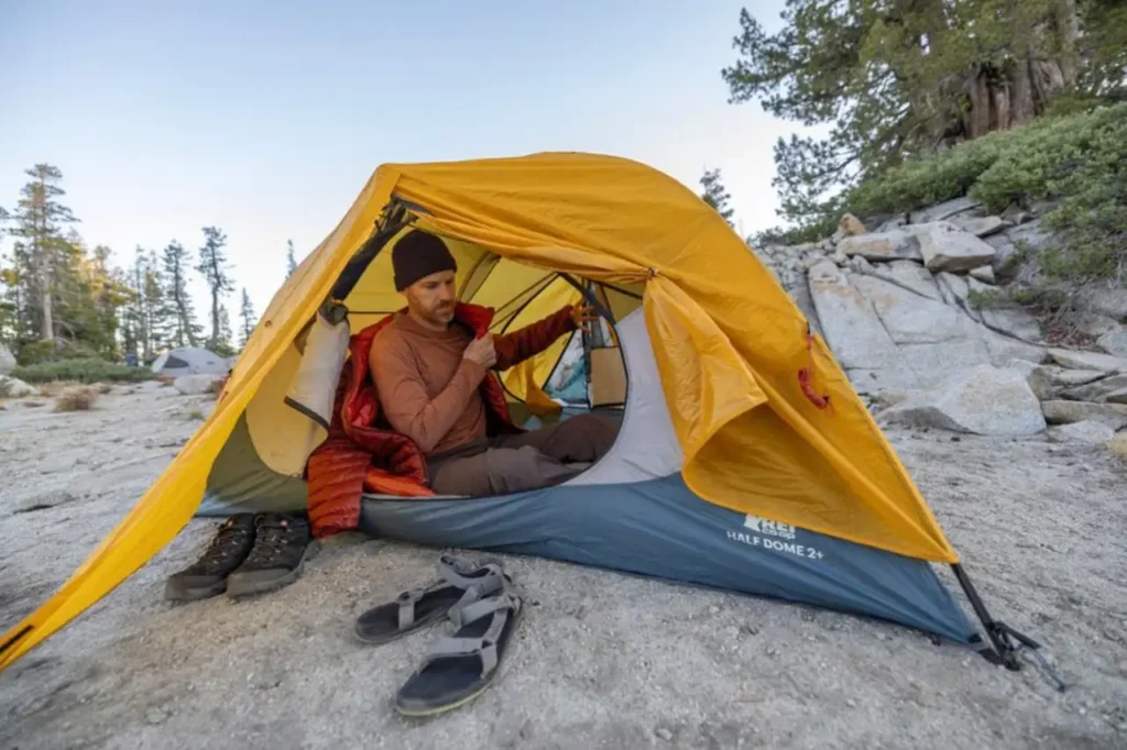 REI Co-op Trail Hut 2 beginner camping tent at a rocky campsite with camper inside, easy setup shelter for first-time campers and one of the best camping tents for beginners