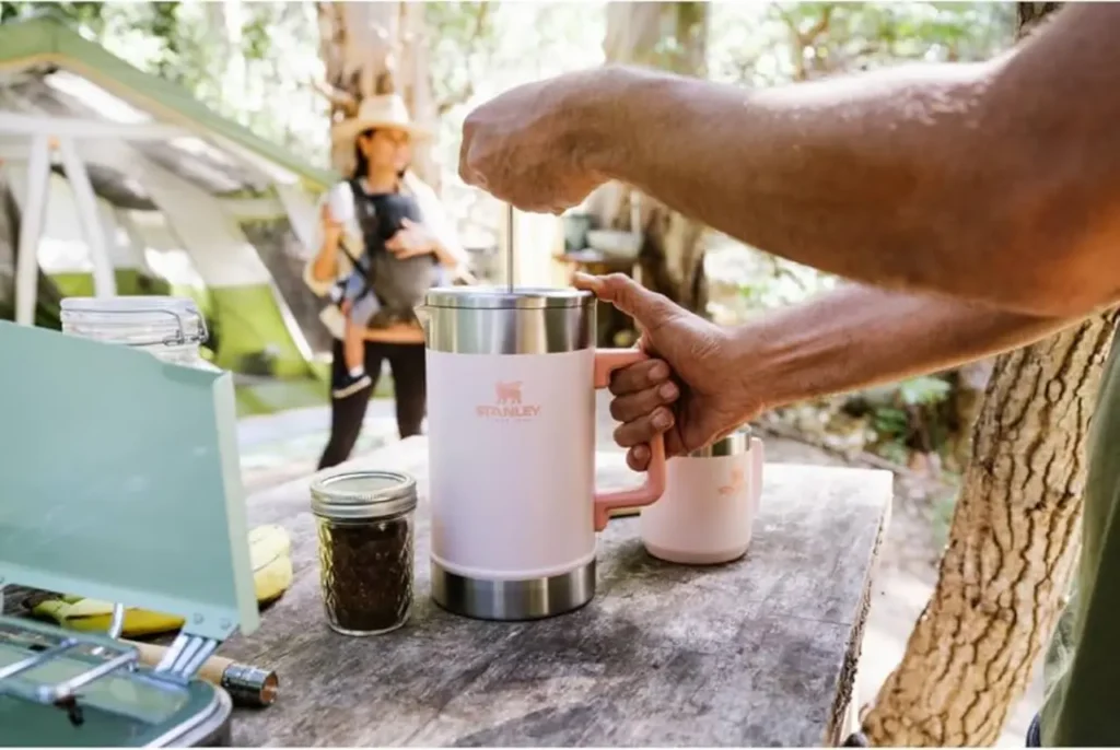 Stanley French press being used to make camp coffee at an outdoor campsite with a tent in the background.