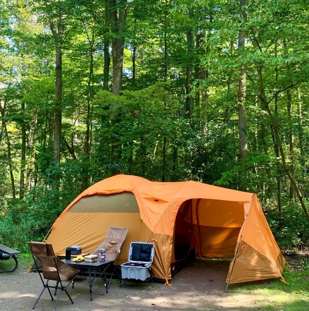 The North Face Wawona 6 tent set up at a forest campsite with camp chairs, table, cooler, and beginner camping gear for a camping packing list for beginners.