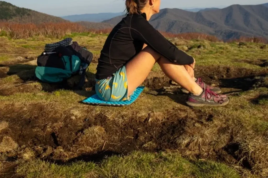 Hiker sitting on a compact blue foam sit pad during a mountain trail break, representing practical outdoor gifts under $25 for hikers and campers.