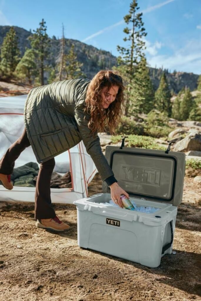 Camper reaching into a YETI cooler beside a tent at a mountain campsite during a car camping trip.