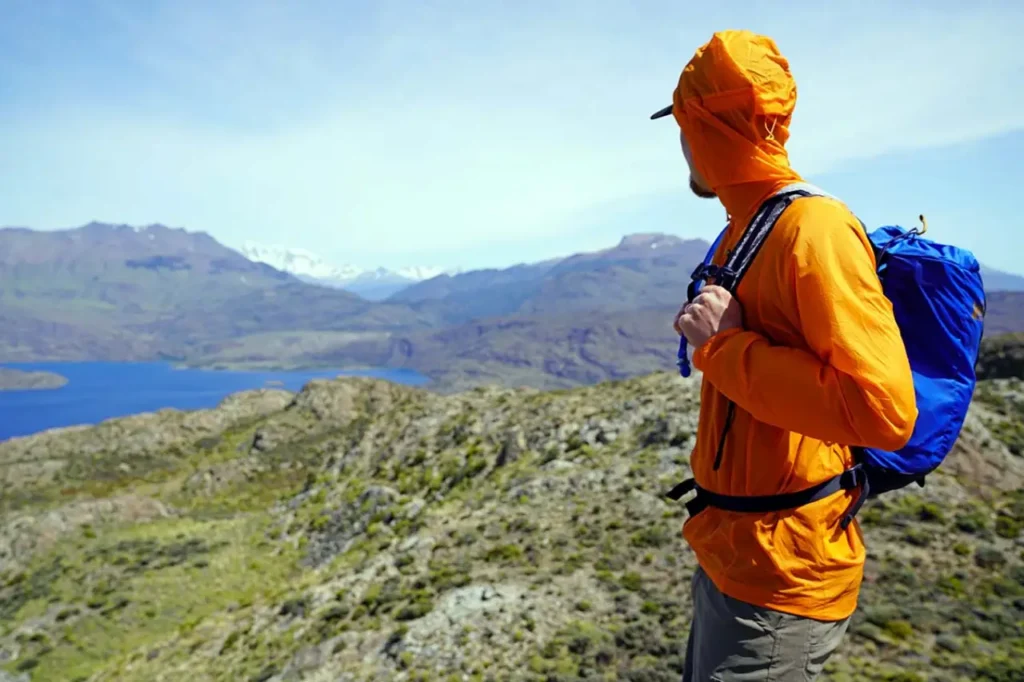 Hiker wearing a Patagonia Houdini windbreaker jacket with a blue backpack on a rocky mountain trail, illustrating what to wear hiking in windy, exposed terrain.