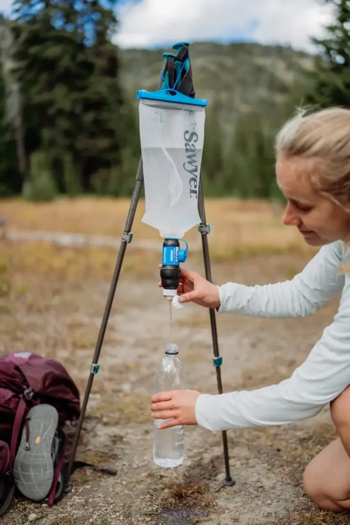 Sawyer Squeeze water filter being used in a gravity setup to fill a plastic bottle during a hiking trip.