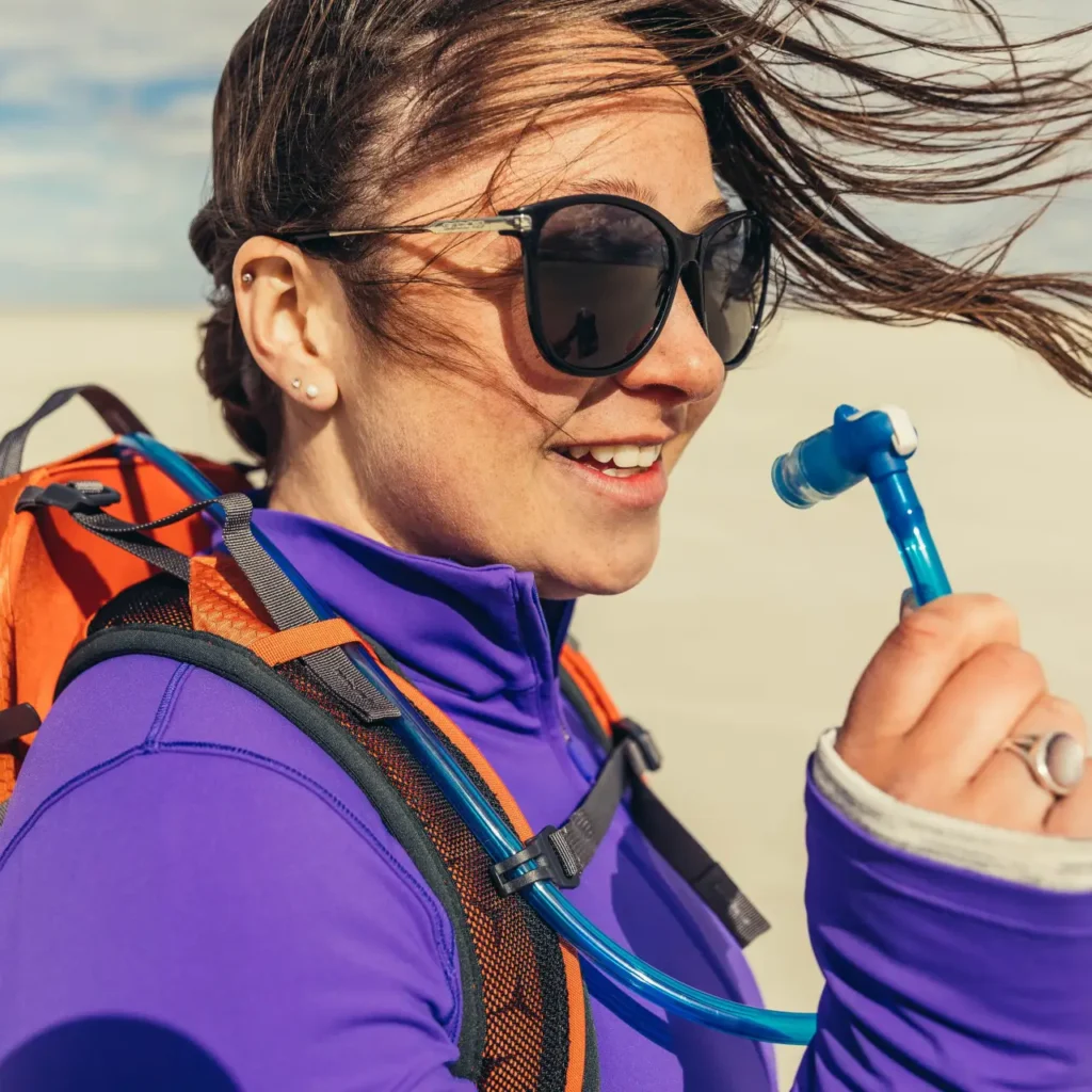 Hiker wearing a hydration pack and holding the drinking tube bite valve during a sunny outdoor hike