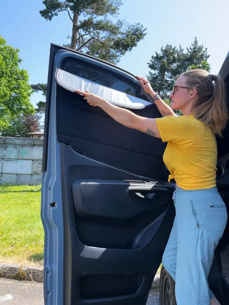 Woman installing an insulated magnetic van window cover on a camper van door for privacy, insulation, and better sleep