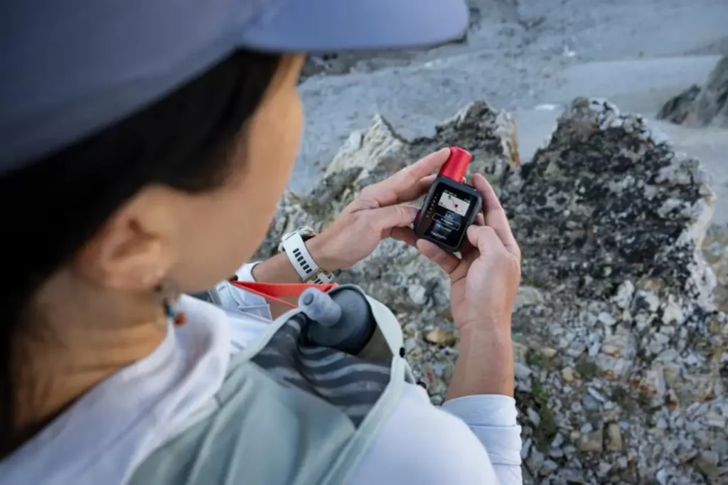 Hiker checking a Garmin inReach Mini 3 Plus satellite communicator while resting on a rocky mountain trail.