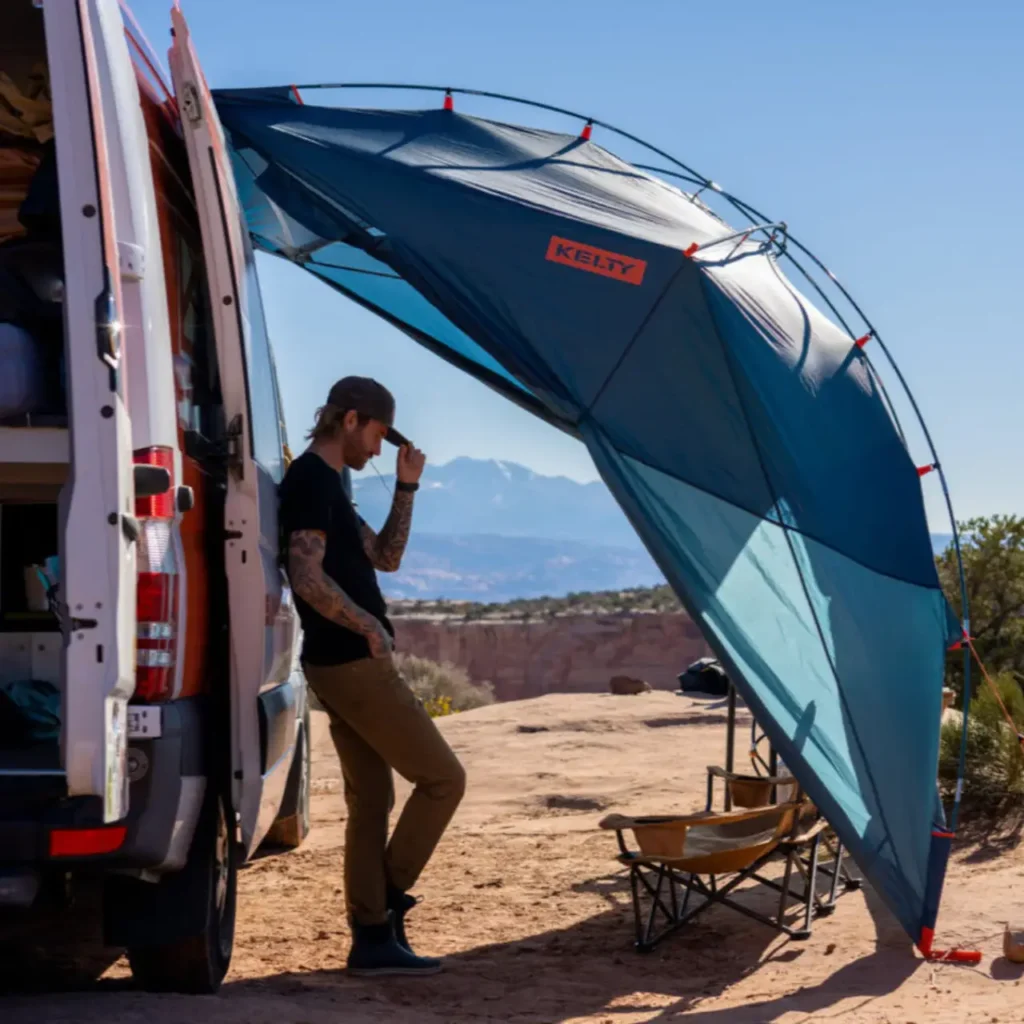 Kelty Backroads Shelter attached to a camper van, providing shade at a summer camping site in hot weather.