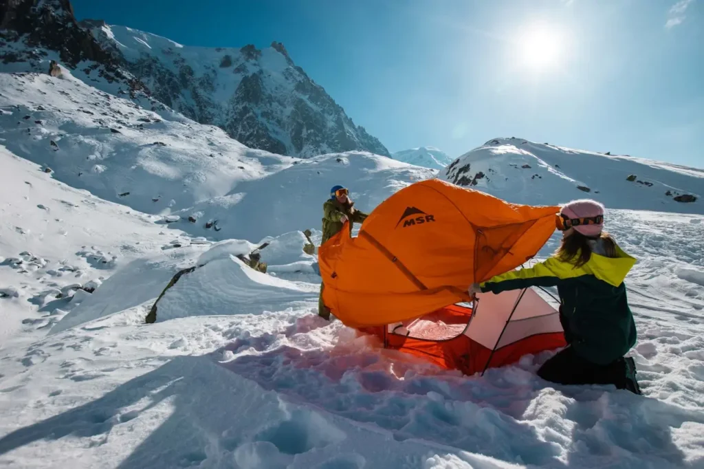 MSR Access 2 Tent being set up by two campers on a snowy alpine campsite for a cold weather camping trip.