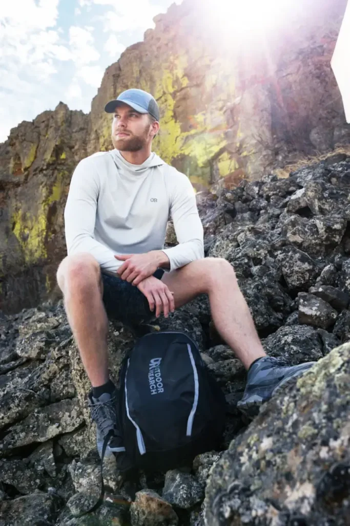 Hiker wearing the Outdoor Research Echo Hoodie while resting on rocky terrain in bright sunlight.