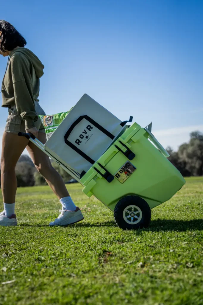 RovR RollR 45 wheeled camping cooler being pulled across grass at a sunny campsite.
