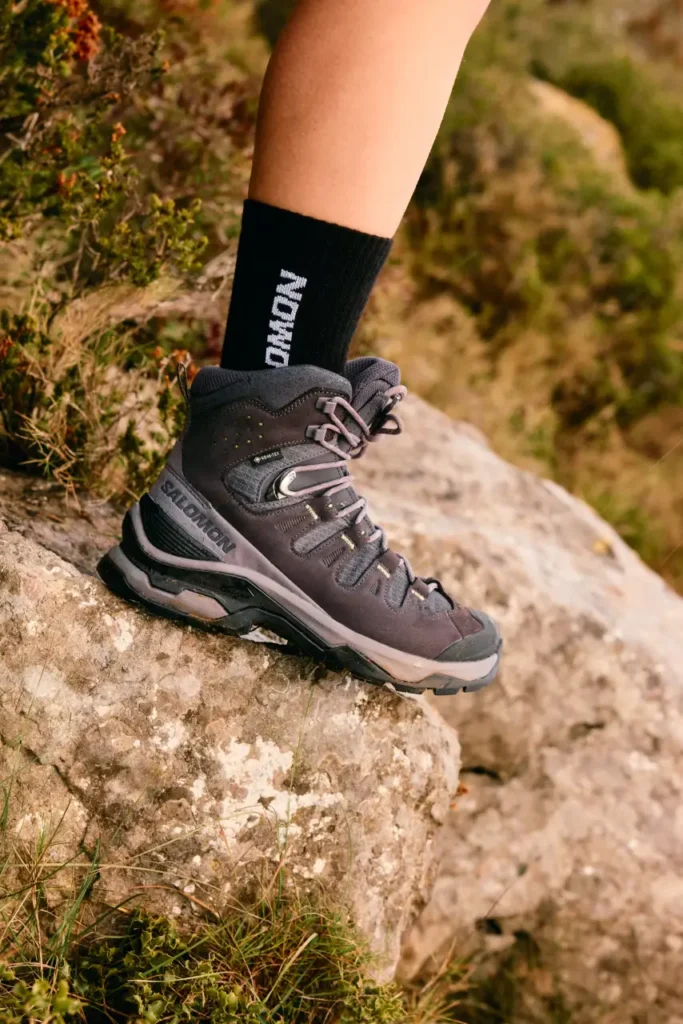 Salomon Quest 5 GTX hiking boot on rocky trail terrain, showing ankle support, rugged lacing, and grippy outsole traction.