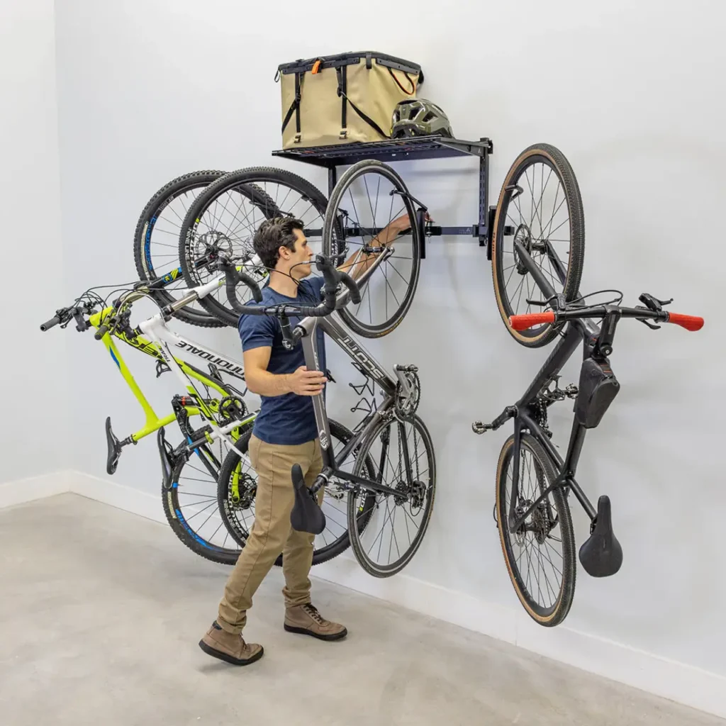StoreYourBoard Swivel Mount Bike Storage Rack holding multiple bicycles vertically on a garage wall with outdoor gear stored on an overhead shelf.