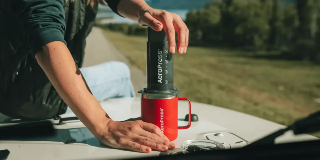 AeroPress XL Coffee Press brewing coffee into a red mug on the hood of a vehicle during a road trip.