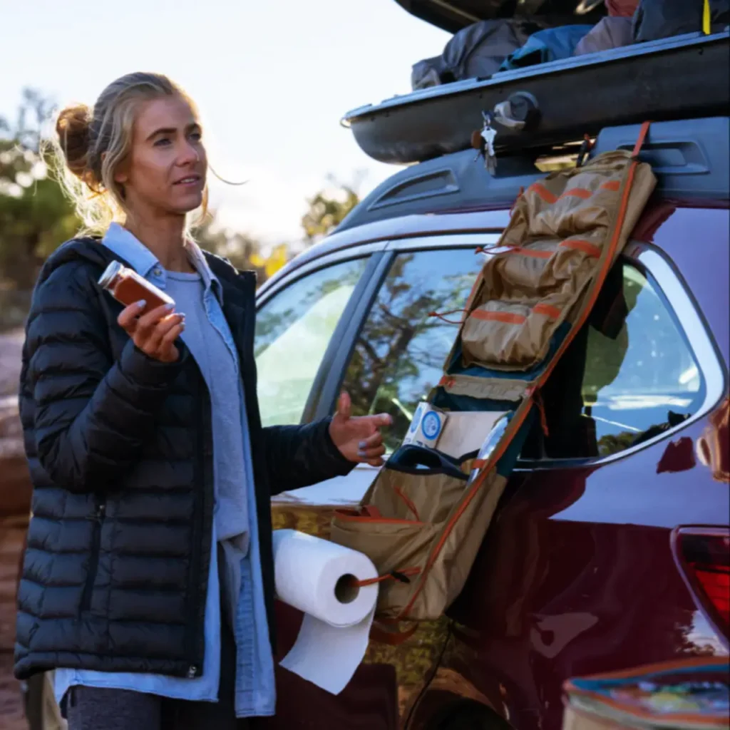 Woman using a Kelty Camp Galley Deluxe Bag attached to the rear of a vehicle during a van camping trip.
