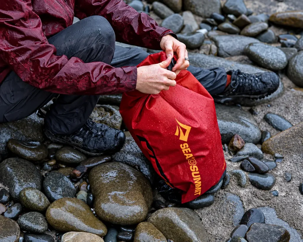 Red Sea to Summit Big River Dry Bag being sealed on wet river rocks to protect camping gear from rain and moisture.
