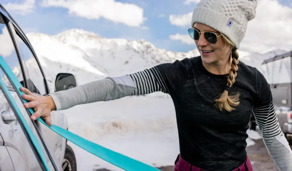 Woman wearing a Smartwool Intraknit Thermal Merino base layer while securing gear beside a vehicle in snowy mountains.