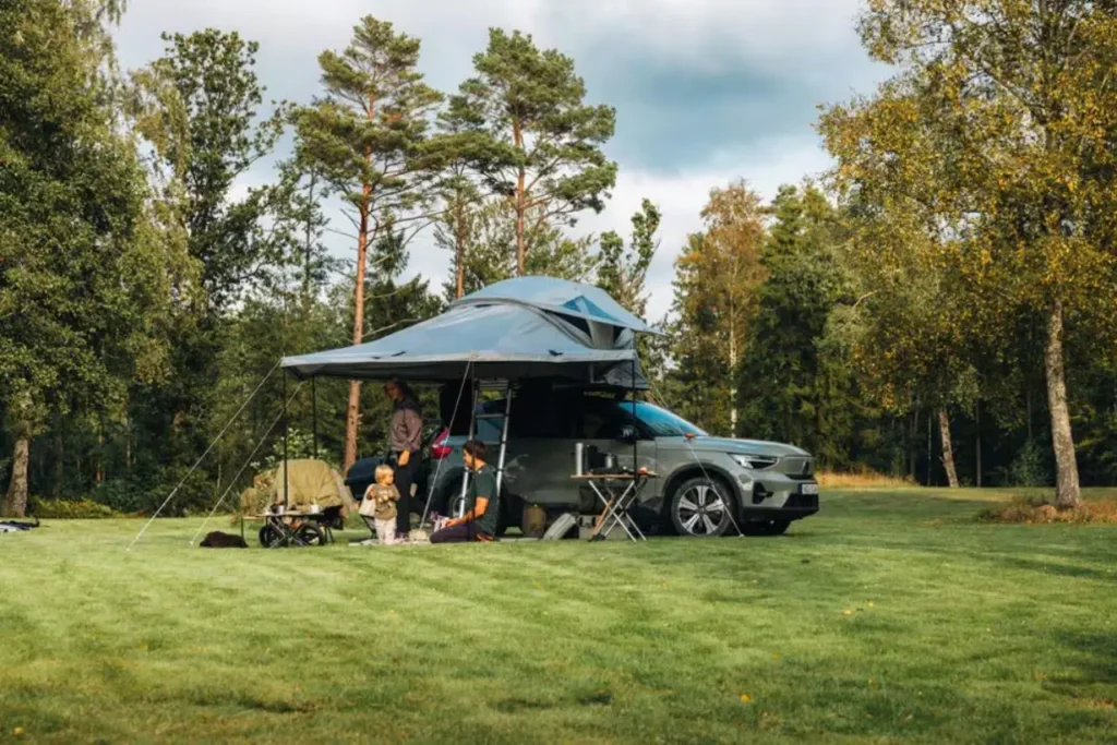 Family camping beside an SUV with a Thule Approach M rooftop tent set up in a wooded campground.