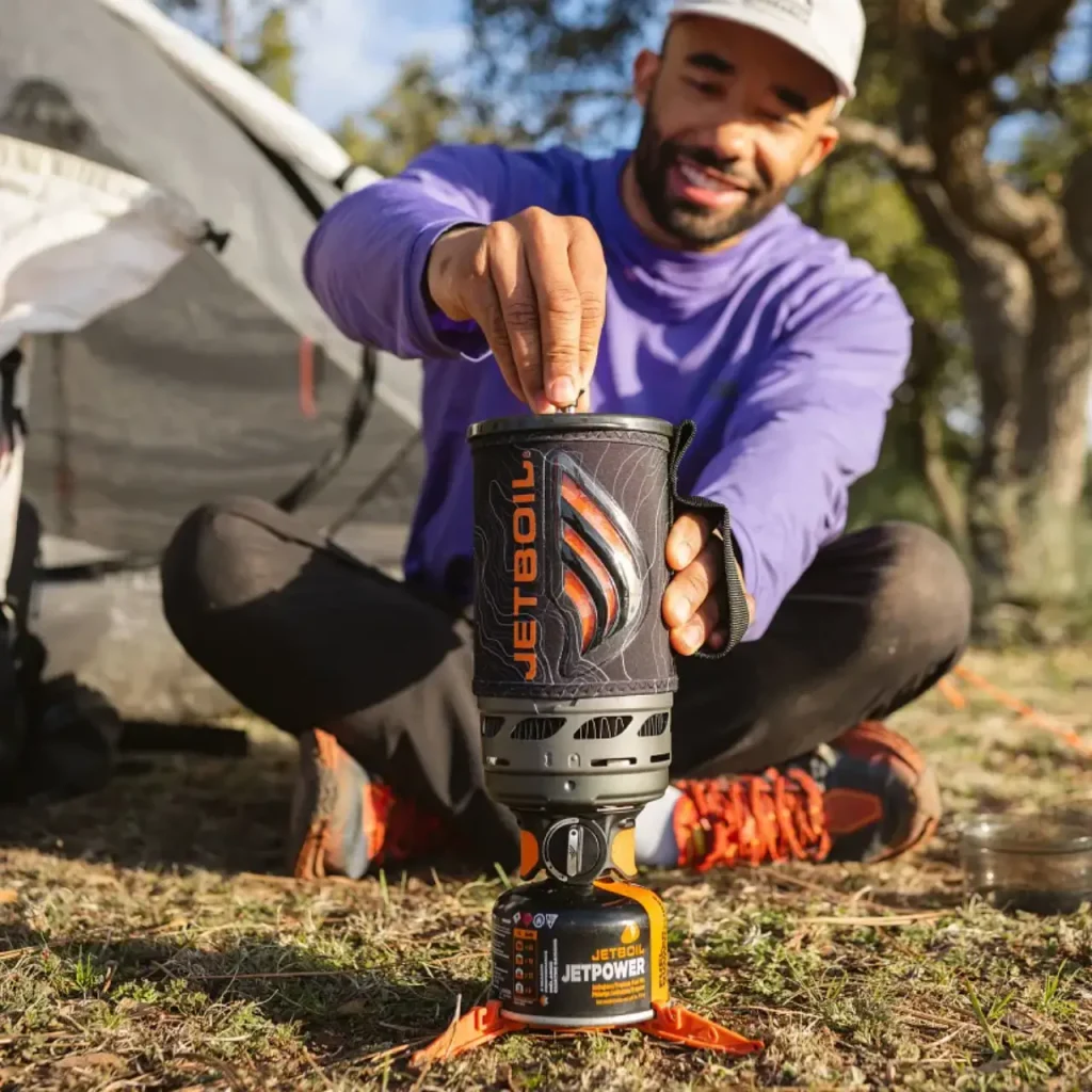 Man using a Jetboil Flash 1.0 L Fast Boil System beside a camping tent, featured in a guide to the best outdoor gifts for him