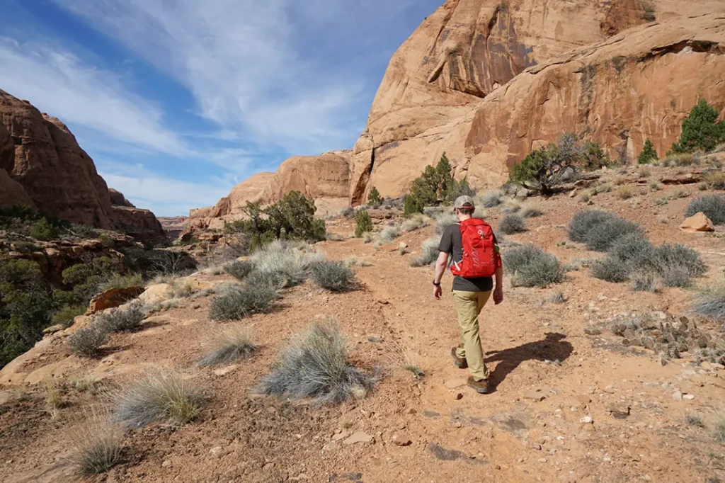 Hiker wearing a red daypack on a desert canyon trail during a weekend hike.