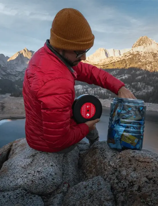 Backpacker opening a BearVault BV500 Journey bear canister filled with food in a mountain campsite.