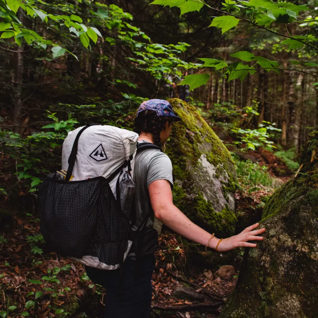 Backpacker hiking through a forest wearing a large backpack on a wooded trail, representing the best backpacking backpacks for multiday trips.