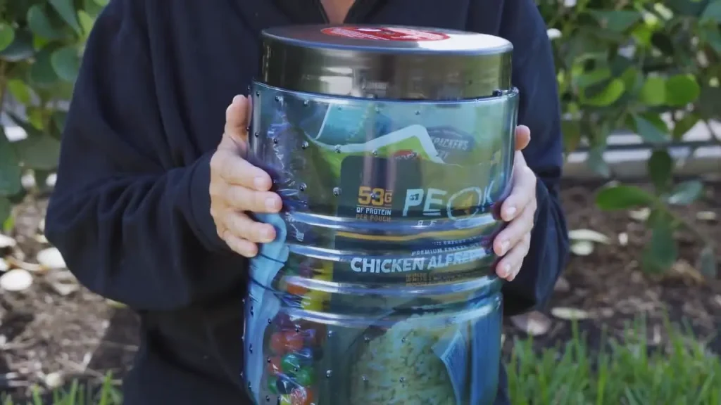 Backpacker holding a transparent bear canister packed with food for a multi-day backpacking trip.