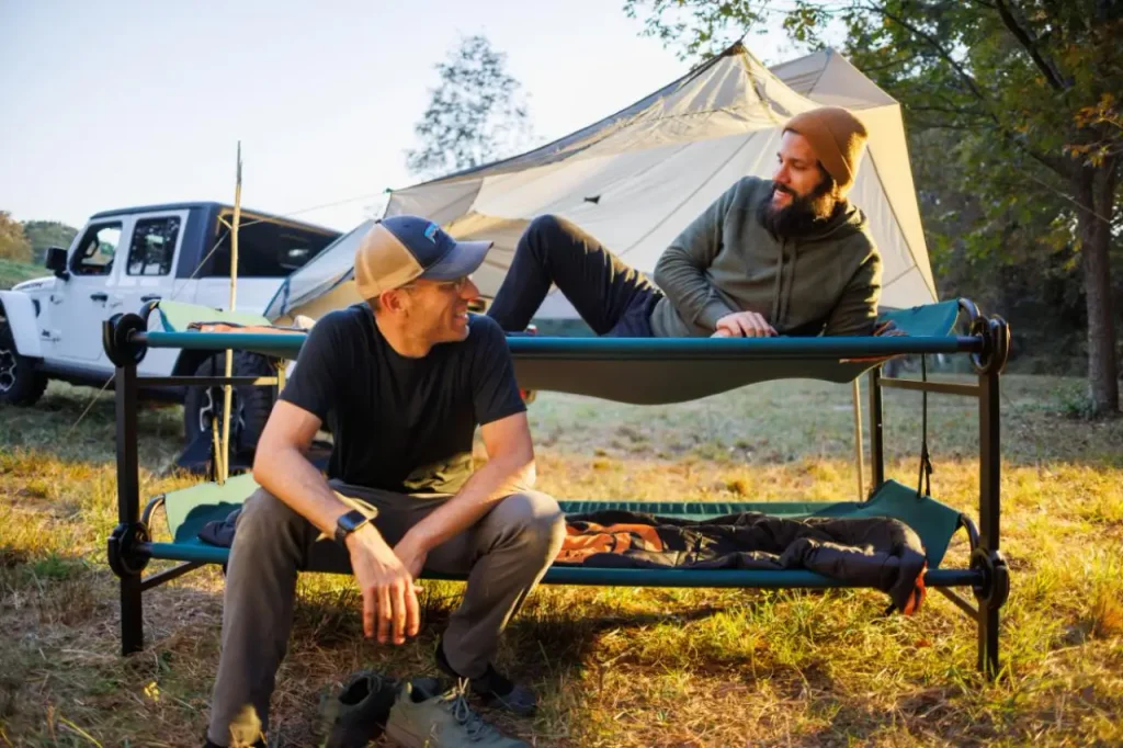 Disc-O-Bed Large Bunk set up at a campsite with two campers relaxing beside a tent and vehicle.