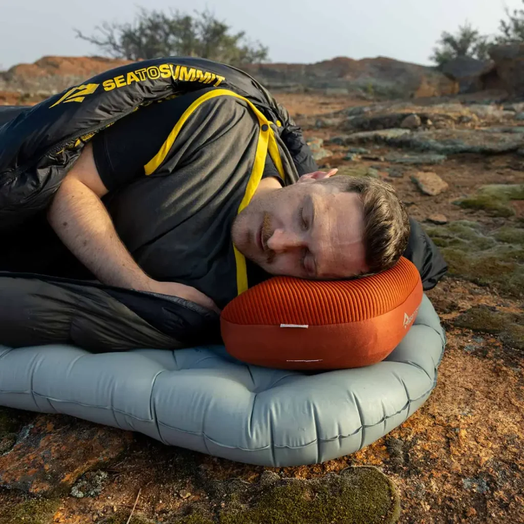 Camper sleeping comfortably on an orange camping pillow and sleeping pad outdoors.