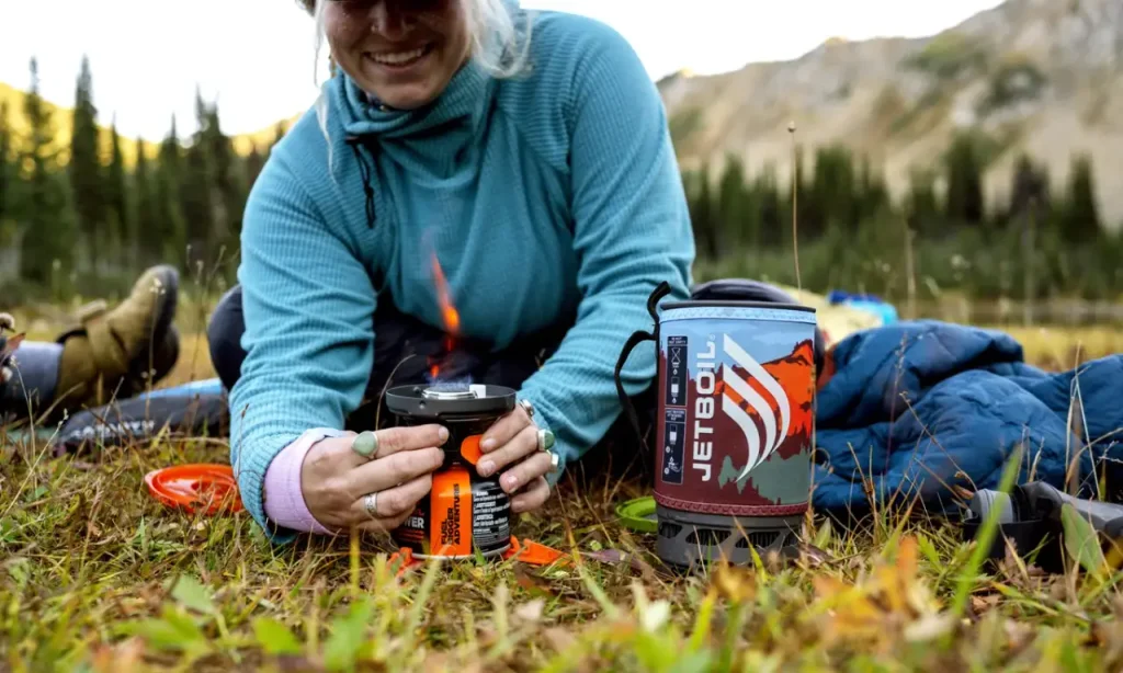 Woman using a Jetboil Flash at a mountain campsite for a guide to the best outdoor gifts for her, including hiking, camping, travel, comfort, and adventure gear.