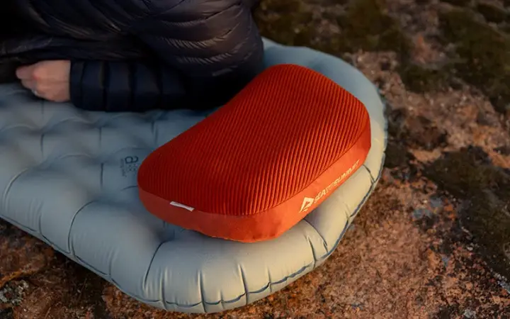 Orange Sea to Summit Aeros Premium camping pillow resting on an inflatable sleeping pad outdoors.