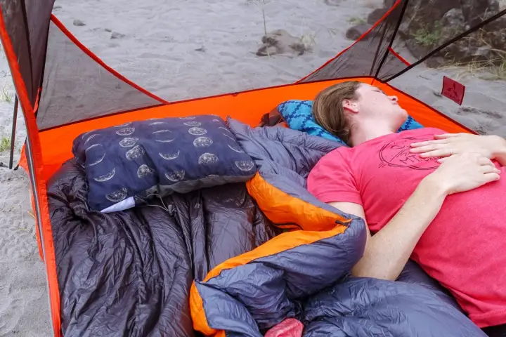 Camper relaxing beside a Therm-a-Rest Compressible Pillow Cinch inside a camping tent.